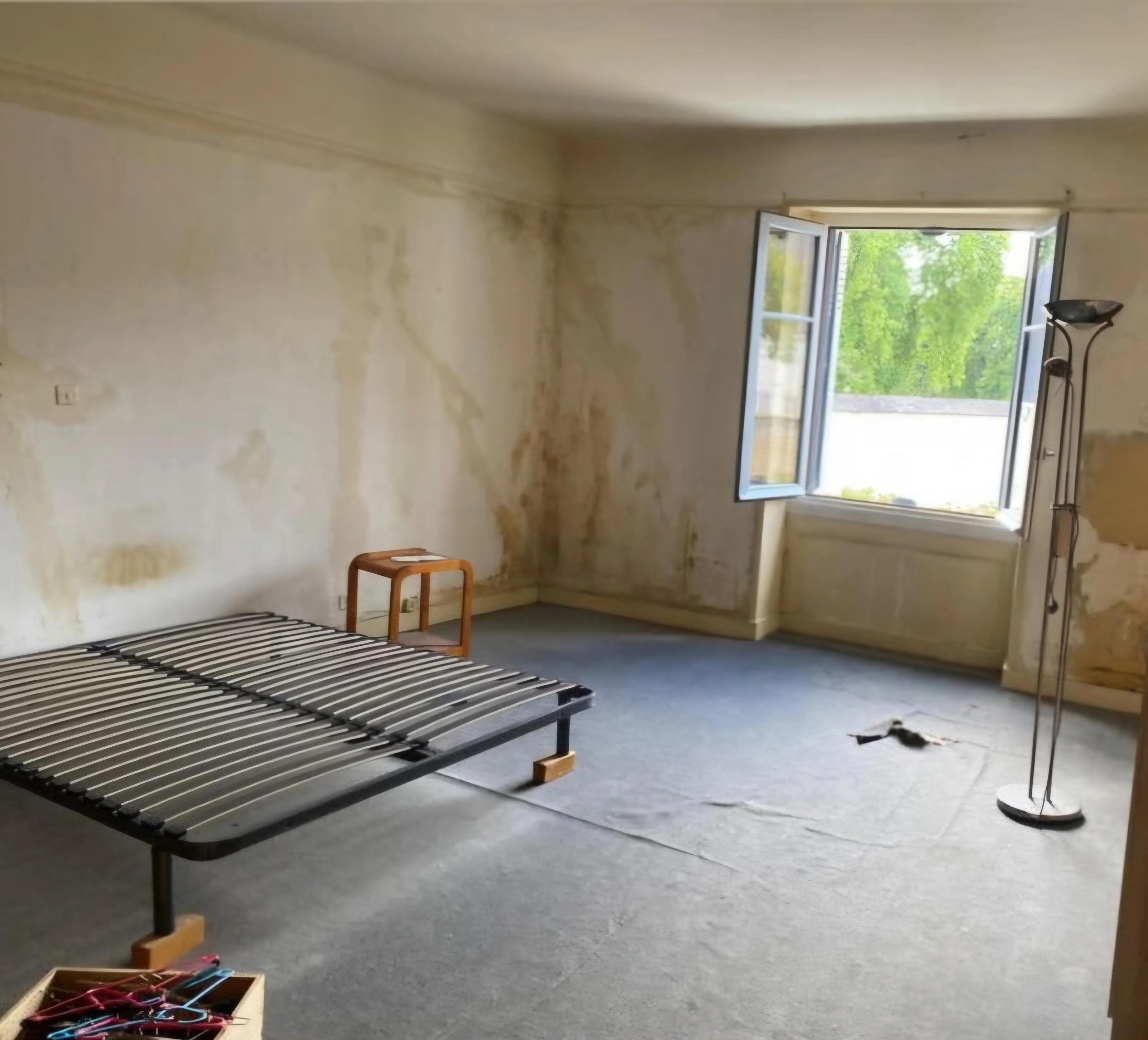 Chambre avant travaux : murs tachés d’humidité, enduit écaillé et sol en béton brut