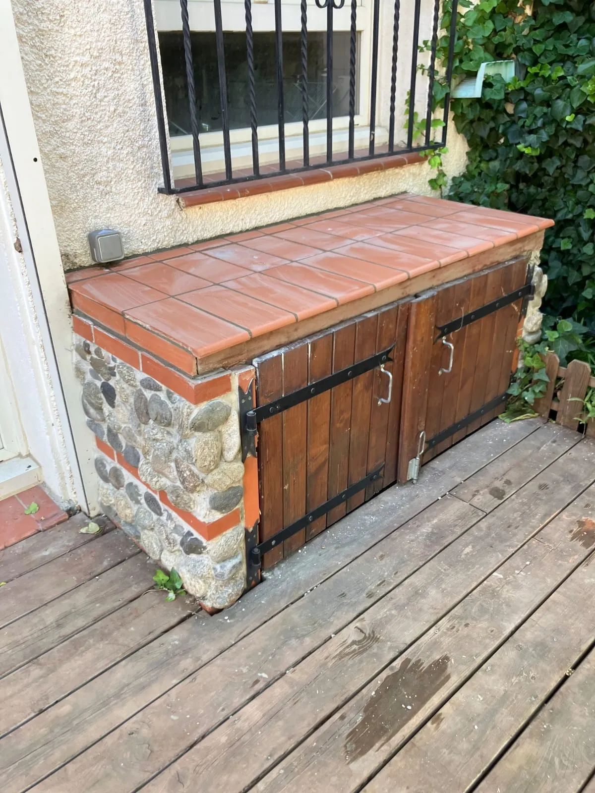 Le même muret après travaux : dessus carrelé en terre cuite et deux portes en bois à pentures noires