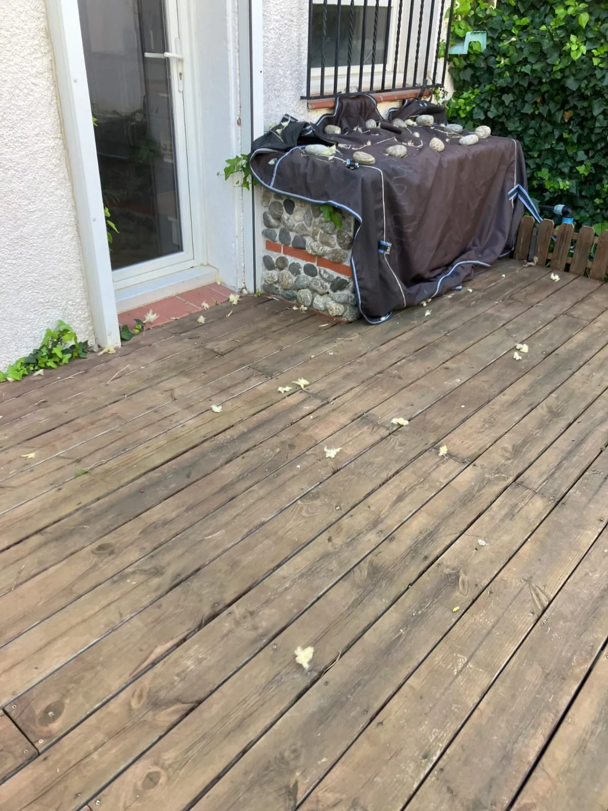 Terrasse en bois avant travaux : muret en galets et briques recouvert d’une bâche tenue par des pierres