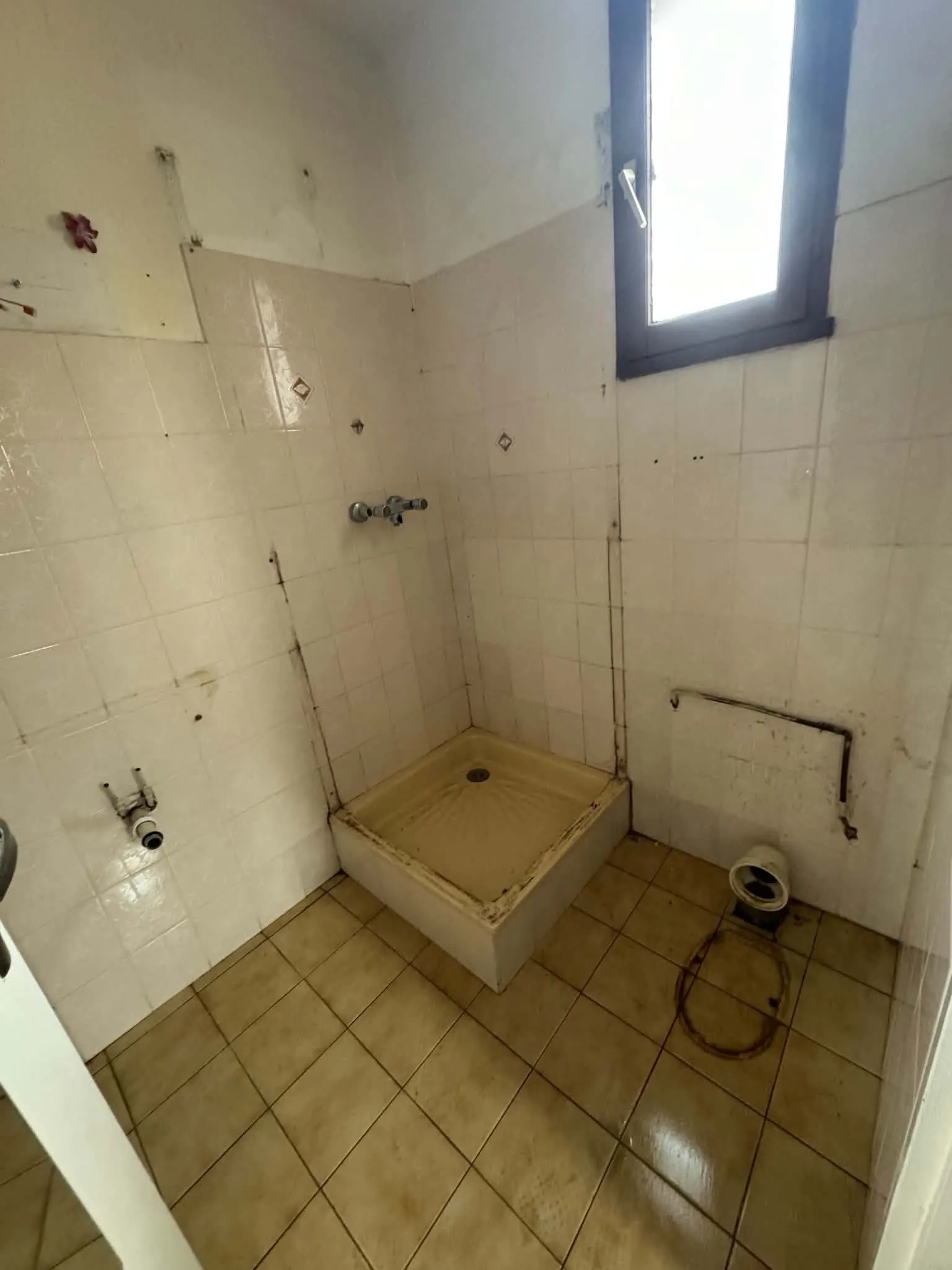 Salle d’eau avant travaux : receveur de douche jauni, joints noircis, sol carrelé taché et évacuation des WC à nu